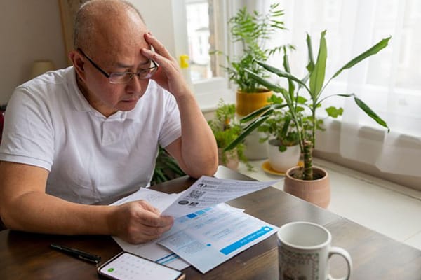 Older Man Reviews Energy Bill While Sitting in Kitchen