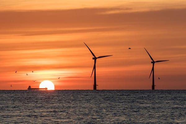 Wind Energy Windmills Under Sunset as Ocean liner in Background